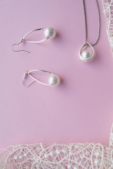 Beautiful silver shiny pearl jewelry, trendy glamorous earrings, chain on pink purple background with exquisite lace. Lay Flat, top view, copy the location of the vertical frame