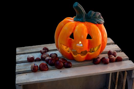 Halloween Pumpkin with Chestnuts Decoration on wooden box, autumn holiday concept,, burning candle seen through nose, candle flickering in wind, isolated on black