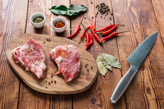 Raw steaks with spices and knife on wooden table. Preparation for lunch.