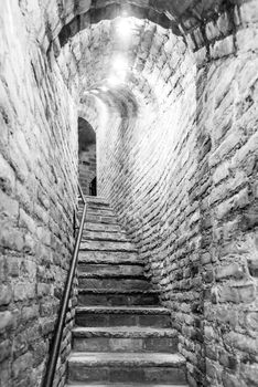 Narrow staircase in old cellar with brick walls. Black and white image.