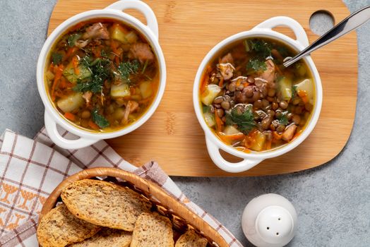 Two plates with lentil soup and chicken on a wooden board, top view.