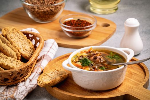 Lentil soup with chicken in a white bowl on a wooden board on a gray table and ingredients.