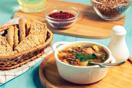 Lentil soup with chicken in a white bowl on a wooden board on a blue table and ingredients.