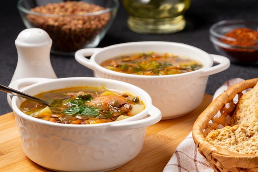 Lentil soup with chicken in a two white bowls on a wooden board on a black table and ingredients.