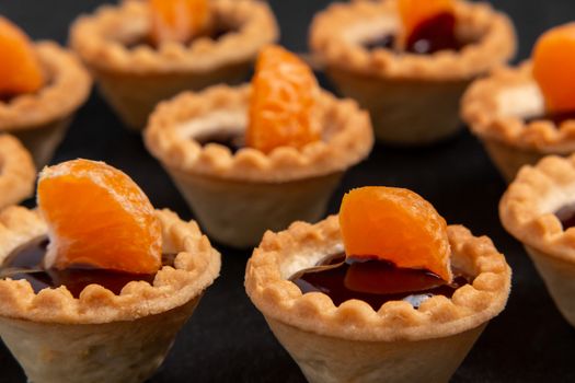 Sweet tartlets with chocolate and slices of tangerine on a dish of natural slate for serving, close-up.
