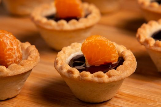 Sweet tartlets with chocolate and slices of tangerine on wooden dish for serving, close-up.