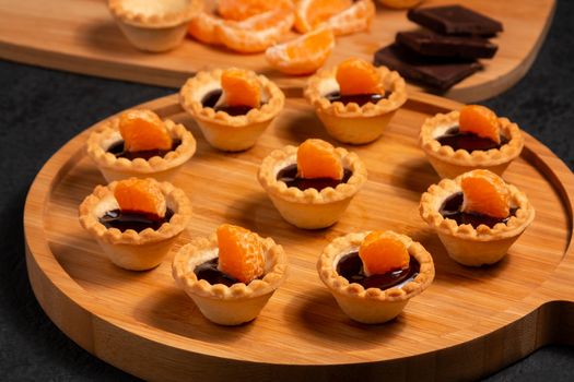 Sweet tartlets with chocolate and slices of tangerine on a wooden dish for serving.
