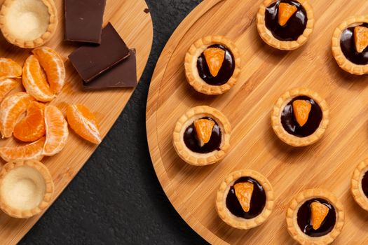 Sweet tartlets with chocolate and slices of tangerine on a wooden dish for serving, top view.