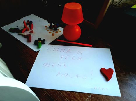Children's creativity, a sheet of paper and a heart symbol from plasticine and a night lamp on the table.