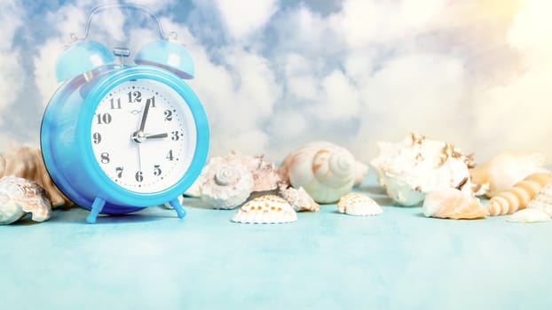 Seashell border and an alarm clock on a blue table against a blue sky with clouds - summer holidays and vacation time concept, copy space, place for text.