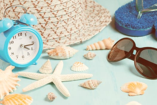 Seashells, alarm clock and beach accessories on a blue table - summer vacation and vacation time concept.