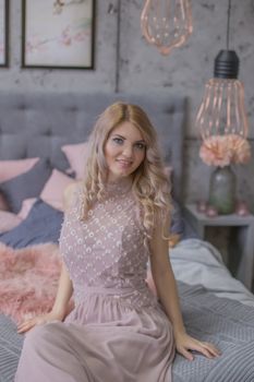 Glamour woman in pink dress sitting in gray and pink bedroom