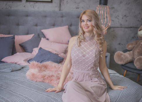 Glamour woman in pink dress sitting in gray and pink bedroom