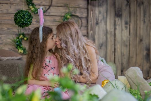 Little child girl wearing bunny ears kissing her mother among Easter decoration in studio