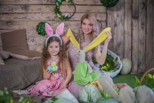 Little child girl wearing bunny ears kissing her mother among Easter decoration in studio