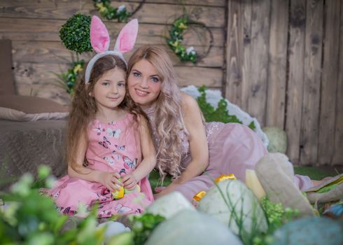 Little child girl wearing bunny ears and her mother among Easter decoration in studio