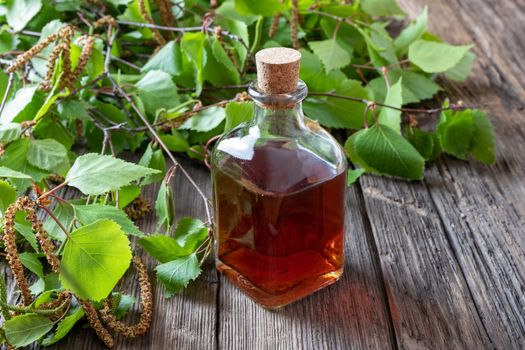 A bottle of tincture with young birch leaves and catkins on a table