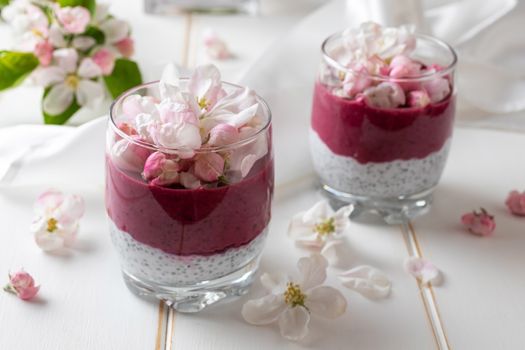 Layered chia pudding with yogurt, blueberries and apple blossoms on a white background