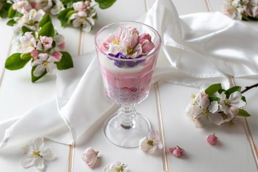 Layered chia pudding with yogurt, red currants and apple blossoms on a white background