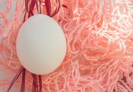 Easter concept, white egg on pink background, woven fabric nest, top view, copy space, bright sunlight