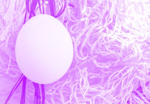 One Easter egg in Easter nest with tinted on lilac-pink background, post-processing effect, copy space, top view, flat lay.