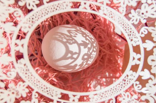 Easter card with egg and white openwork oval frame on coral background, Bright sunlight creates beautiful shadows on white egg, copyspace, top view