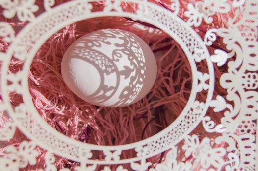 Easter card with egg and white openwork oval frame on coral background, Bright sunlight creates beautiful shadows on white egg, copyspace, top view