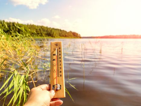 Thermometer showing 30 degrees Celsius of heat against the background of the lake water and the blue sky in sunlight.