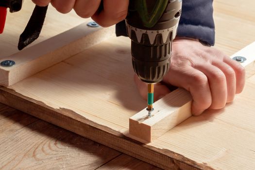 Male hands screw wooden blocks to the boards with a screwdriver.