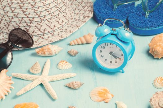 Seashells, alarm clock and beach accessories on a blue table - summer vacation and vacation time concept.