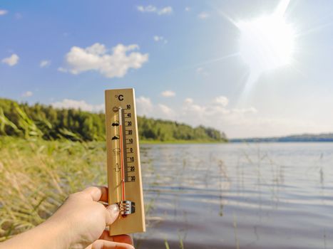 Thermometer showing 30 degrees Celsius of heat against the background of the lake water and the blue sky in sunlight.