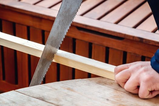 Men's hands sawing a wooden bar with a hacksaw.