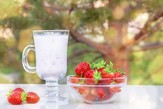 Fresh ripe strawberries in a bowl and iogurt on a white table outdoors on a summer day.