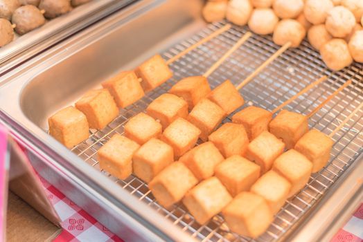 Close-up, selective focus of skewers with fried tofu cubes at farmer market stand in America. Tofu breaded, vegetarian food