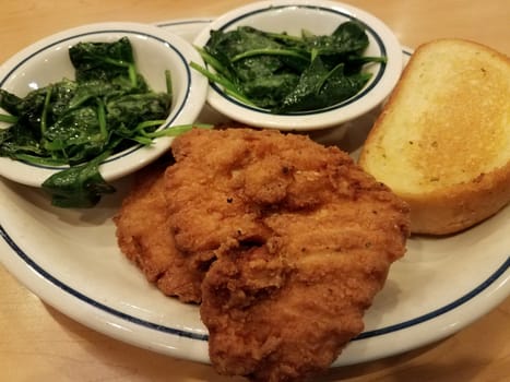 fried chicken and spinach on plate on wood table with bread