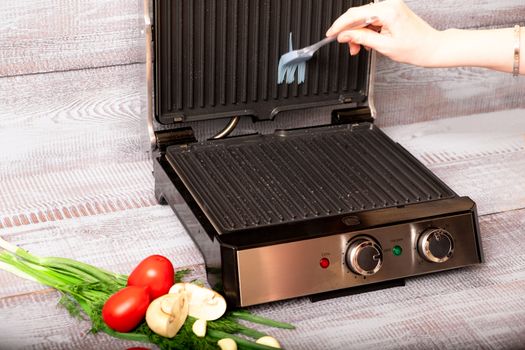 Beef is cooked on the electric grill. Around the grill vegetables laid out. On a wooden background.