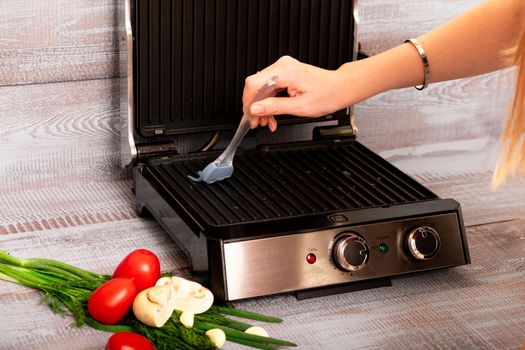 Beef is cooked on the electric grill. Around the grill vegetables laid out. On a wooden background.