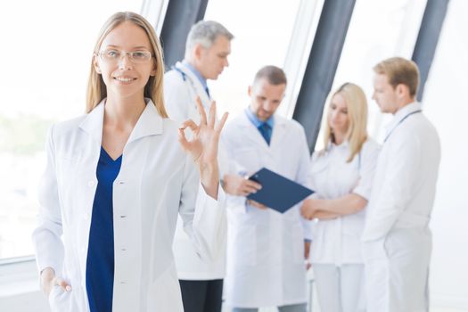 Female doctor showing Ok sign , team of doctors on background