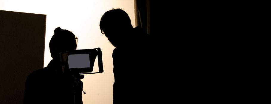 Shooting studio behind the scenes in silhouette images which film crew team working for filming movie or video with professional lighting and equipment such as camera, tripod, soft box, monitor