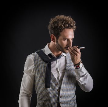 Handsome man sending voice recording or note on cell phone, on black background in studio shot. Looking away