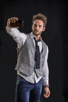 Handsome man taking selfie photo on cell phone or mobile, on black background in studio shot. Looking away