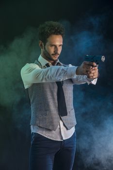 Elegant man with gun, pointing it at someone off frame, on smoky dark background