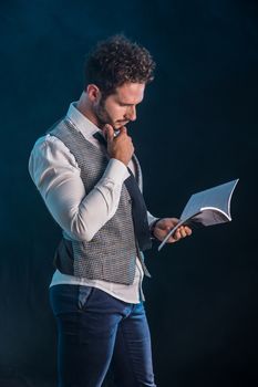 Elegant man reading a book in studio shot, standing on black background