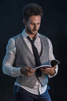 Elegant man reading a book in studio shot, standing on black background