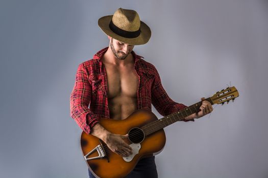 Studio portrait of handsome bearded man with unbuttoned shirt playing guitar over grey background.