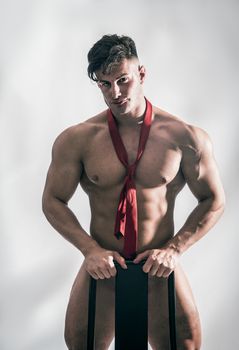 Muscular bodybuilder standing behind chair, totally naked, looking at camera