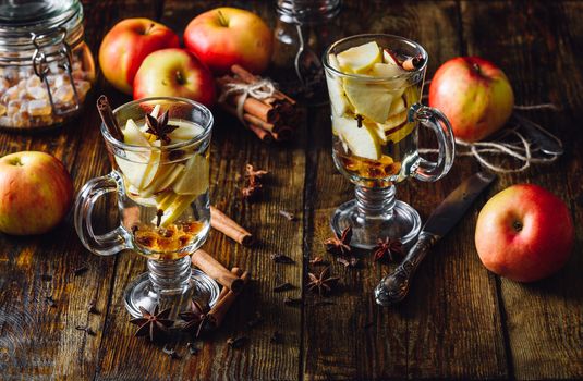 Glasses of Christmas Apple Drink with Clove, Cinnamon, Anise Star and Dark Candy Sugar. All Ingredients and Some Kitchen utensils on Wooden Table. Vertical.