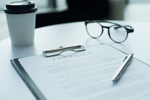 A pair of glasses , pen , coffee and contract lying on top of table