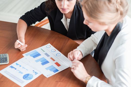 Business women pointing at diagrams discussing financial reports at workplace