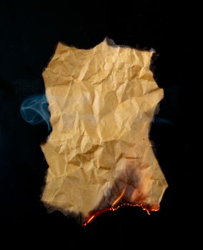 burning piece of crumpled paper on black background